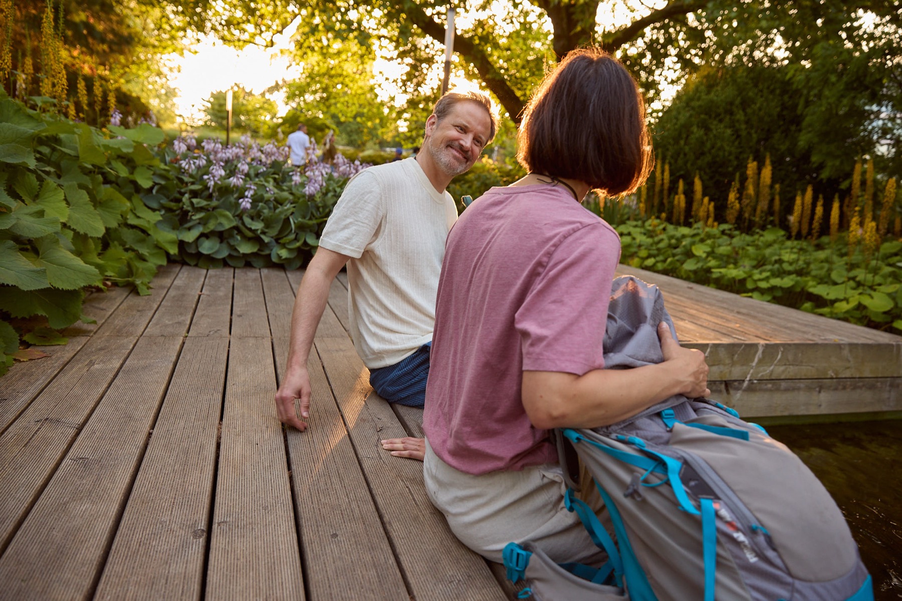 Zwei Menschen im Gespräch auf einer Holzterrasse im Garten, im Abendlicht